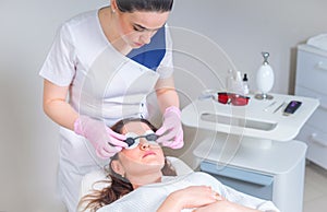 Young woman receiving laser treatment in cosmetology clinic. Eyes covered with protection glasses