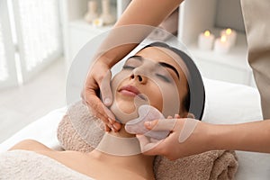 Young woman receiving massage with gua sha tool in beauty salon
