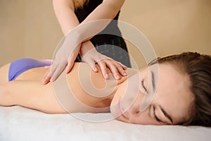 Young woman receiving a neck and shoulders massage done by a masseuse in a spa salon