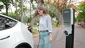 Young woman recharge EV electric car's battery in national park. Expedient