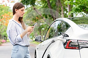 Young woman recharge EV electric vehicle battery from EV charging station. Exalt