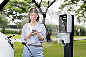 Young woman recharge EV electric vehicle battery from EV charging station. Exalt