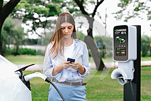 Young woman recharge EV electric vehicle battery from EV charging station. Exalt