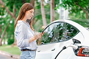 Young woman recharge EV electric vehicle battery from EV charging station. Exalt