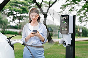 Young woman recharge EV electric vehicle battery from EV charging station. Exalt