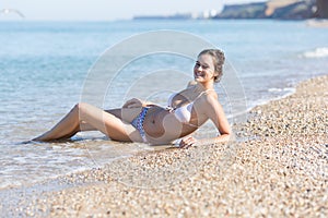 Young woman reclines leaning on elbow on pebbles on beach