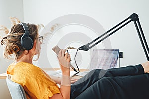 Young woman recording podcast on his laptop computer with headphones and microphone