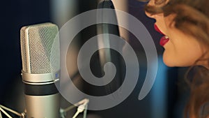 Young woman recording a song in a professional studio. Profile of a woman with a beautiful face and red lips