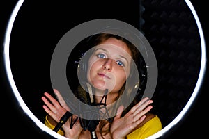 A young woman in a recording Studio on a black background. The girl writes an audio song for the microphone in the headphones,