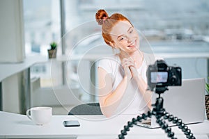 Young woman recording video on camera mounted on tripod for her vlog