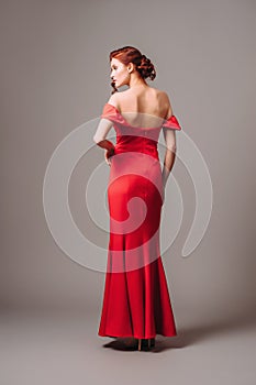 Young woman in red backless dress with arm cuffs on grey studio background.