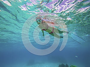 Young woman in red bikini Freediver gliding underwater over vivid coral reef