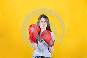 Young woman with red boxing gloves stands in fighting position. Portrait of determined girl prepared for battle isolated on yellow