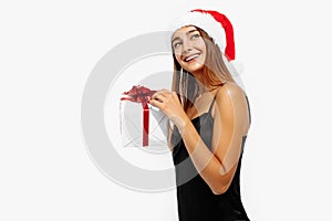 Happy young woman in red Christmas hat and black dress holding a gift box on a white background, Concept of Christmas, holiday