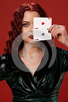 Young woman with a red curly hair holding aces, on a red background. Poker