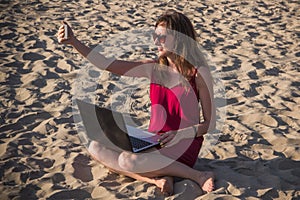 Young woman in red dress with computer and smartphone on the beach. Freelance and downshifting concept.