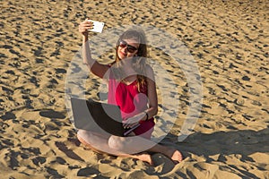 Young woman in red dress with computer and smartphone on the beach. Freelance and downshifting concept.