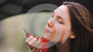 A young woman in a red dress in a red car paints her lips red. Red lipstick