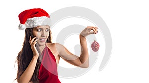 A young woman in a red dress and Santa hat holds a Christmas tree toy in her fingers.  over white background