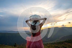 Young woman in red dress standing on grassy field on a windy evening in autumn mountains enjoying view of nature