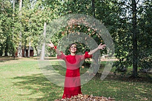 Young woman in red dress. Toss the autumn leaves upward.