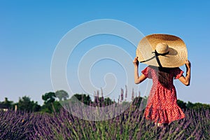 Young woman in red dress and wide-brimmed hat walks among lavender field