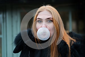 Young woman with red hair make a bubble of gum