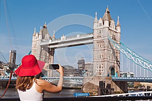 Young woman with red hat taking a photo of the Tower bridge in London