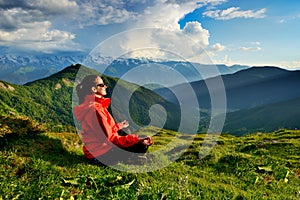 Young woman in red jacket sitting in yoga pose in mountains