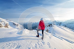 Young woman in red jacket in snowy mountains at sunset in winter