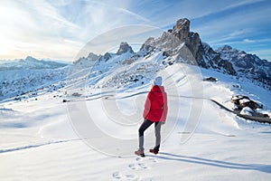 Young woman in red jacket in snowy mountains at sunset in winter