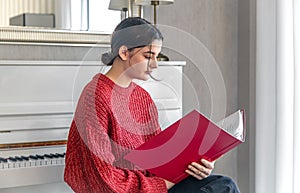 A young woman in a red knitted sweater near a white piano.