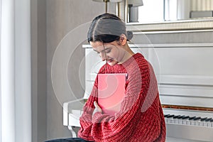 A young woman in a red knitted sweater near a white piano.