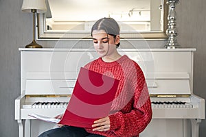 A young woman in a red knitted sweater near a white piano.