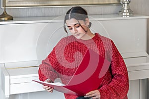 A young woman in a red knitted sweater near a white piano.