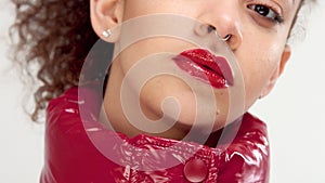 Young woman with red lacquer lips and red shiny jacket on white in studio