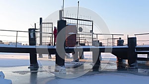 Young woman in red long jacket walks on snow-covered pier standing on bank of frozen river