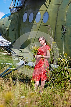 Young woman in a red pin up dress with a bunch of yellow wildflowers stands by an airplane