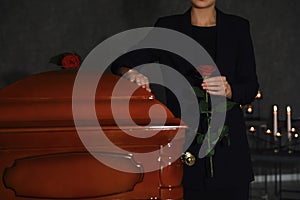 Young woman with red rose near casket in funeral home,