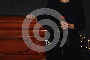 Young woman with red rose near casket in funeral home