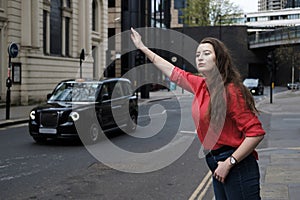 Young woman in red shirt hailing a taxi in urban London