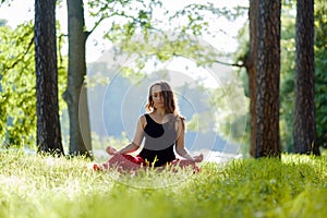 Young woman in red skirt enjoying meditation and yoga on green grass in the summer on nature