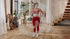 A young woman in red sportswear performs a warm-up before training. A brunette woman stands on a carpet in the middle of