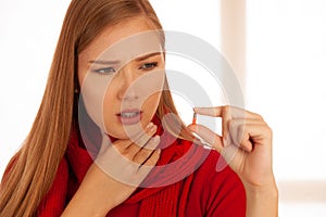 Young woman in red sweater holds pills in her hand as she is ill