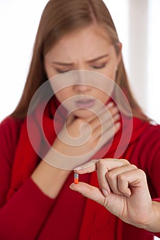Young woman in red sweater holds pills in her hand as she is ill