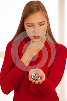 Young woman in red sweater holds pills in her hand as she is ill