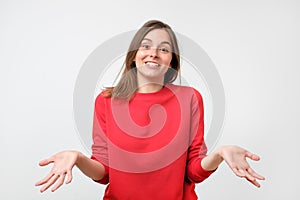 Young woman in red sweater standing disorientated bewildered isolated on gray wall background. Decision making concept.