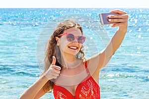 Young woman in red swimsuit is taking self-portrait at the sea background. Beach concept