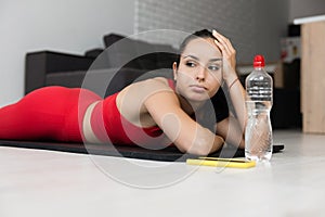 Young woman in red tracksuit doing exercise or yoga at home. Tired bored slim girl lying on her stomach. Rest and relax