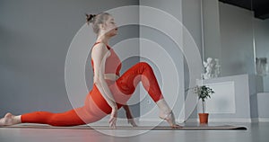 Young woman in red tracksuit sitting on the yoga mat and leaning forward to her feet, person does physical training